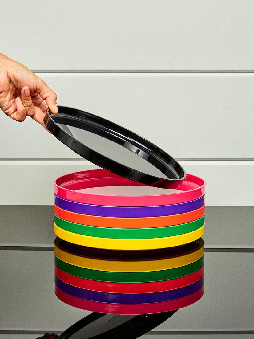 A rainbow stack of dinner plates by Heller with a hand holding up the top plate at an angle.