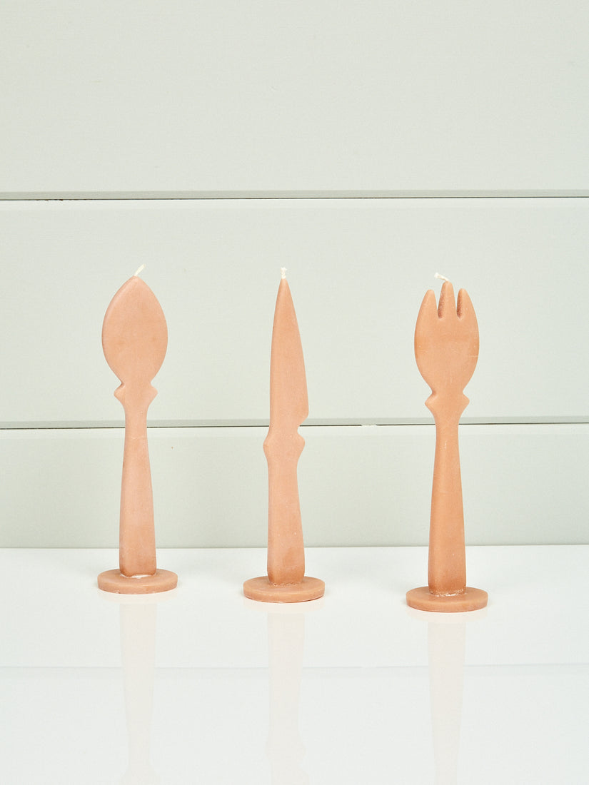 Three beige candles in the shape of a flat spoon, knife, and fork.