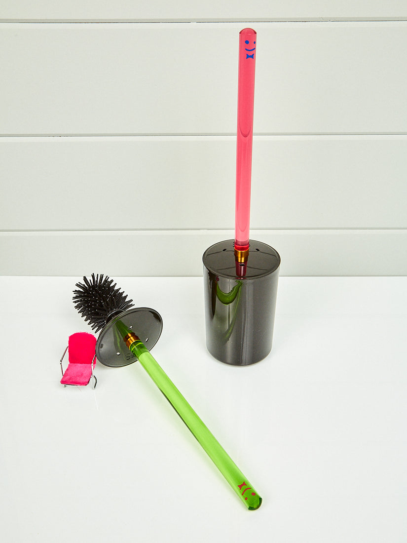 A pink toilet brush by Staff and a green toilet brush laying on its side.