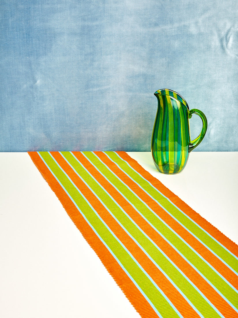 The Saffron Stripe Runner by Dusen Dusen next to a green and yellow striped glass jug.