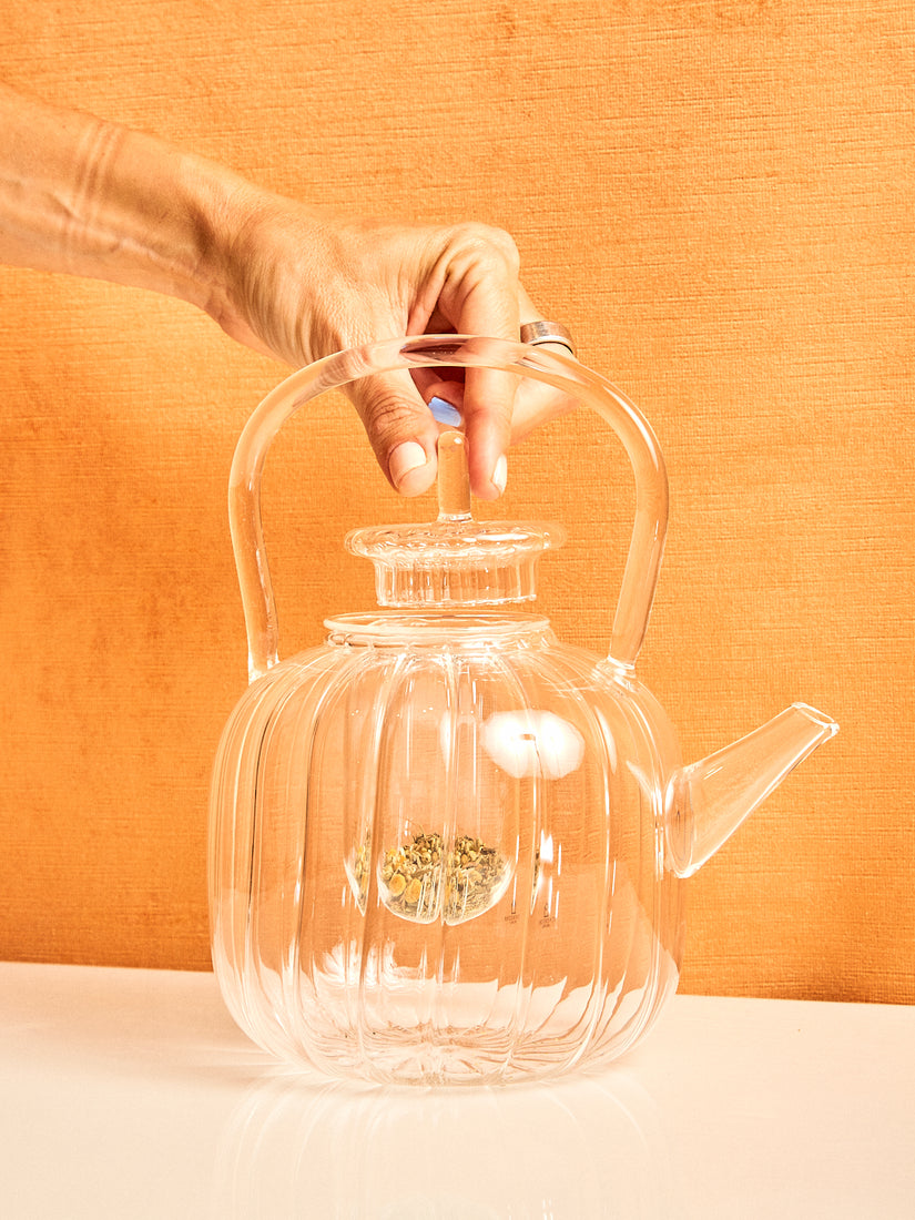 A hand gently lifts the lid of the glass teapot with filter by Ichendorf Milano.