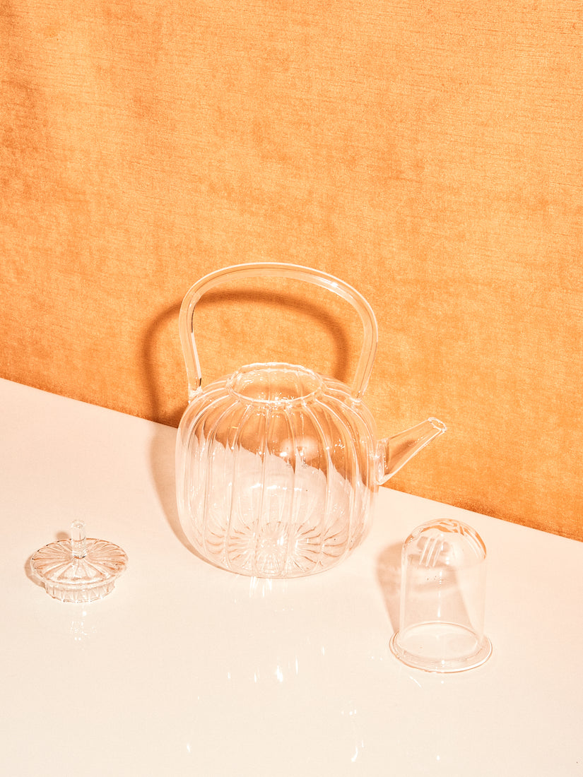 The Teapot by Ichendorf Milano disassembled, it's lit and glass filter sit next to its entirely glass body.