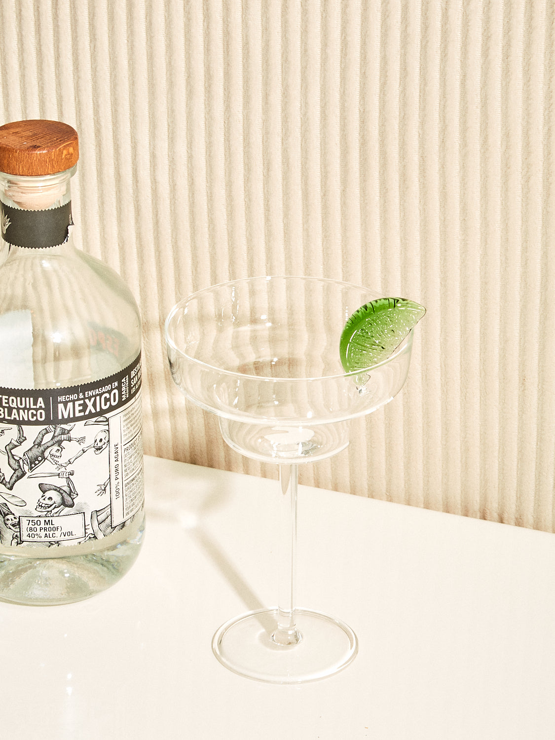 A bottle of tequila sits left of a Margarita Glass by Maison Balzac.