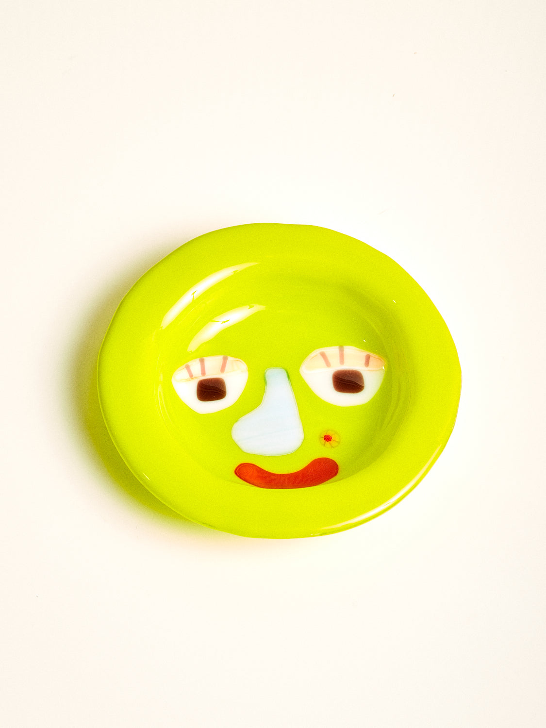 A lime green glass bowl with a graphic face featuring a blue note, red mouth, and flower shaped beauty mark.