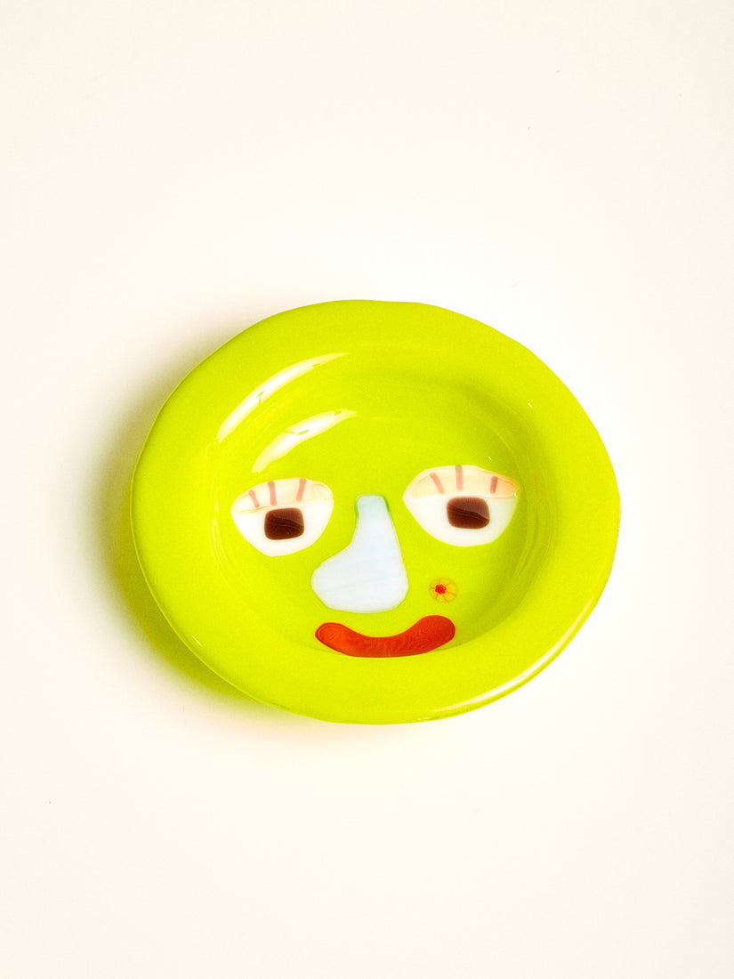 A lime green glass bowl with a graphic face featuring a blue note, red mouth, and flower shaped beauty mark.