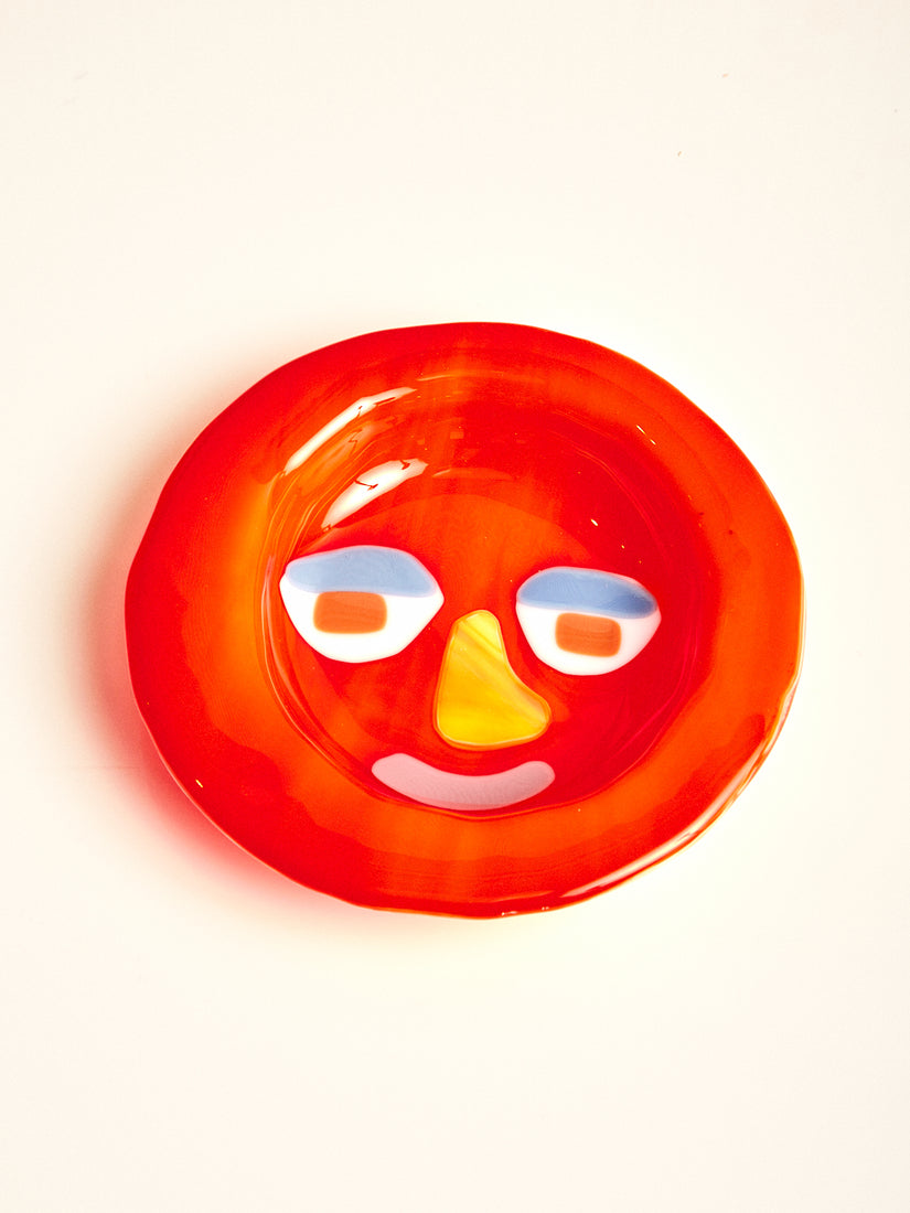 A bright red bowl with abstract face featuring a yellow nose, and pink mouth.