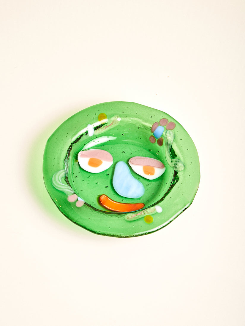 A transparent grass green bowl with abstract flowers and a face design.