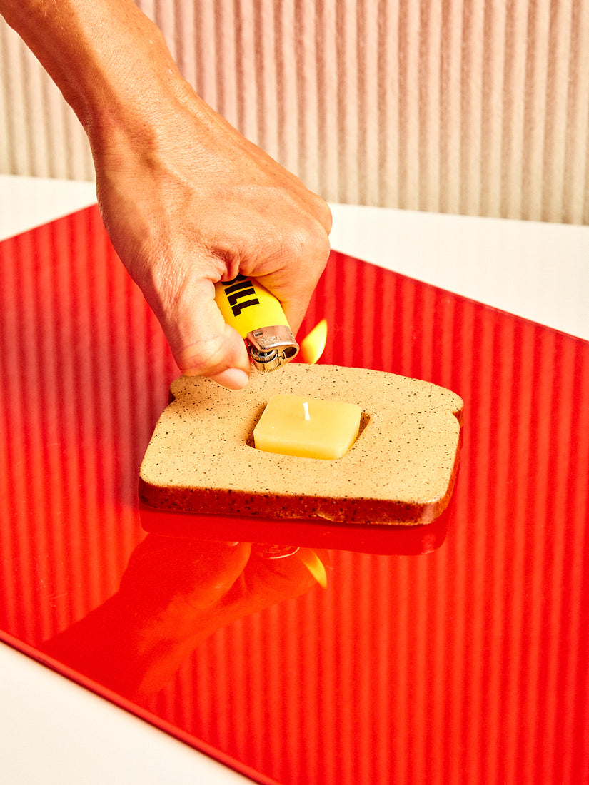 A hand lights the Butter Toast candle with holder.