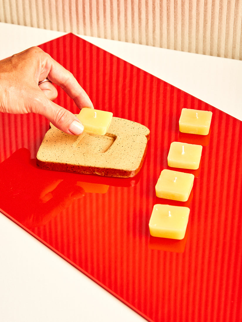 A hand places a butter pat candle into the toast candle holder. Four extra pats of butter sit right.