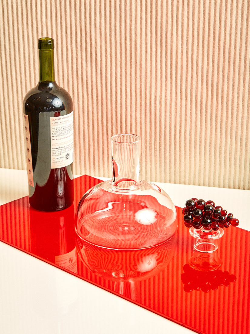 A bottle of wine, the Bordeaux Wine Decanter, and it's stopper sitting in a line.