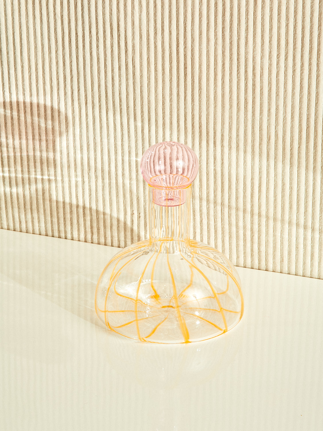 The Grand Soleil Decanter by Maison Balzac with a pink bulbous stopper and yellow striped body.