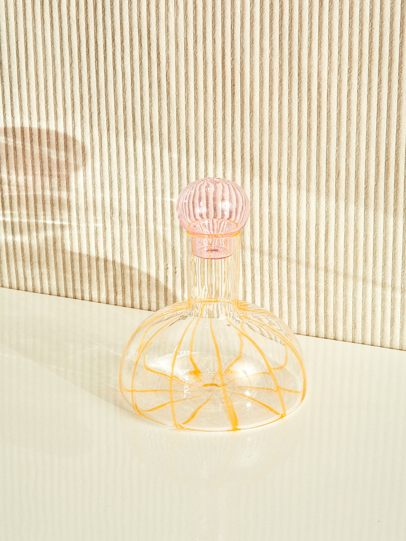The Grand Soleil Decanter by Maison Balzac with a pink bulbous stopper and yellow striped body.