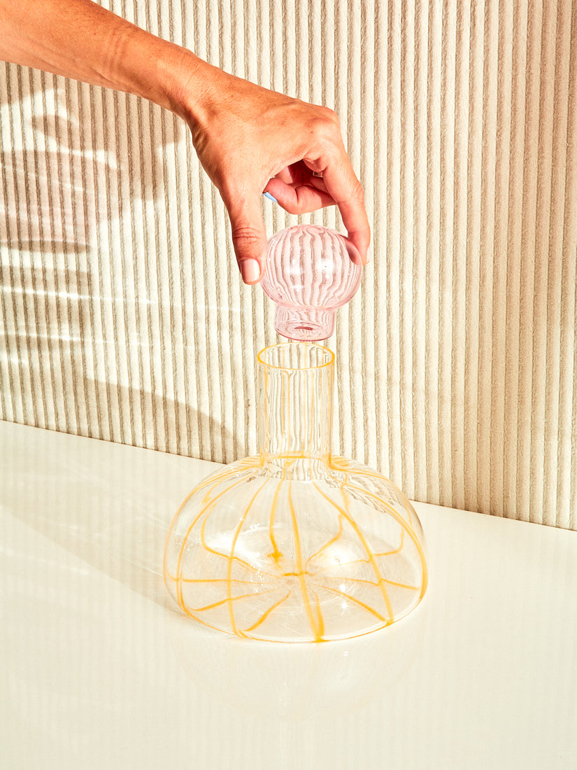 A hand holds up the round pink stopper of the Grand Soleil Decanter by Maison Balzac.