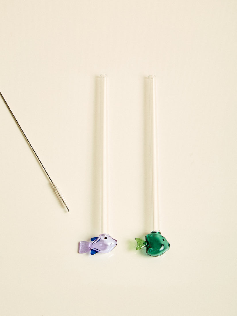 A pair of straws, one with a lilac fish at the bottom, one with a green fish at the bottom.