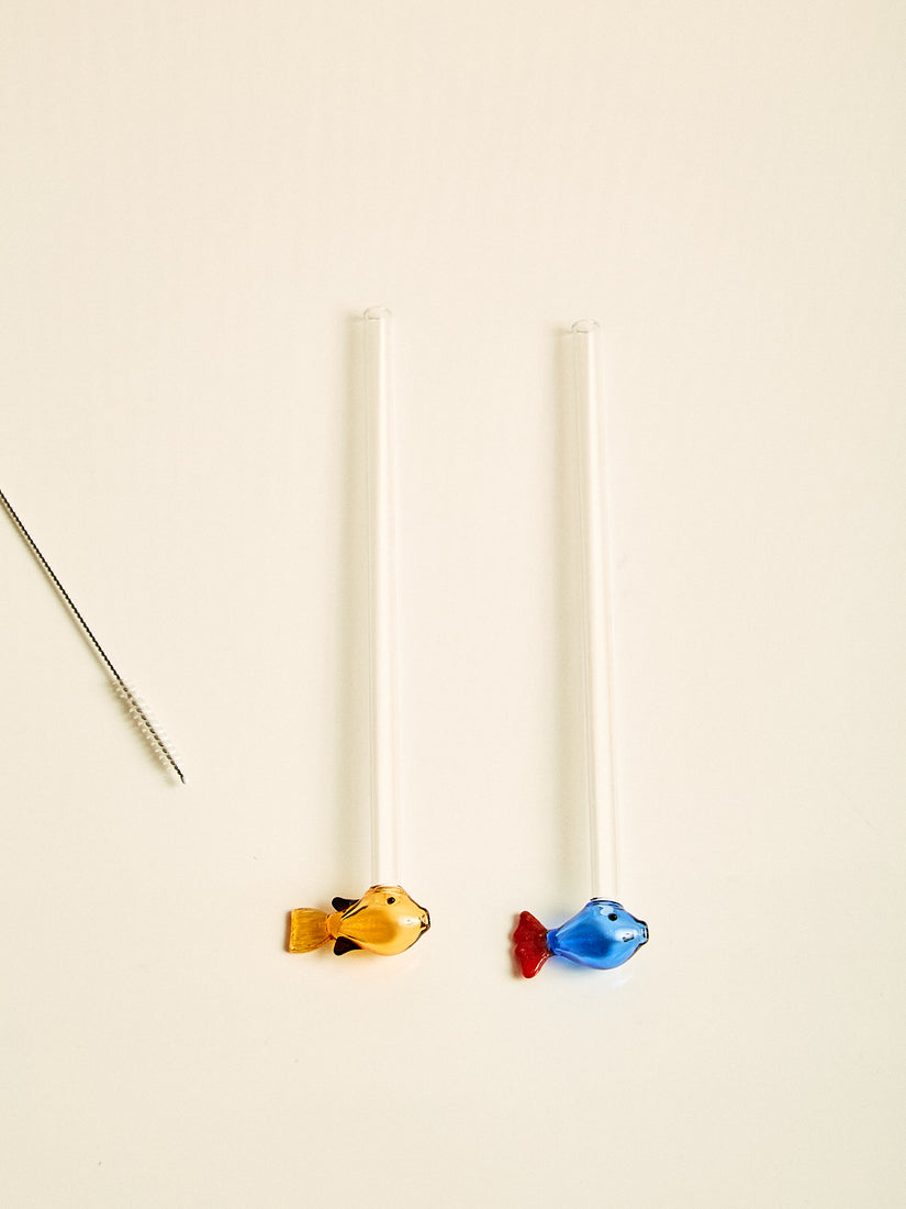 A pair of straws, one with an amber fish at the bottom, one with a blue fish at the bottom.