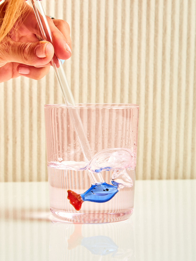 Someone blows bubbles into a glass of water through a blue and red fish straw.
