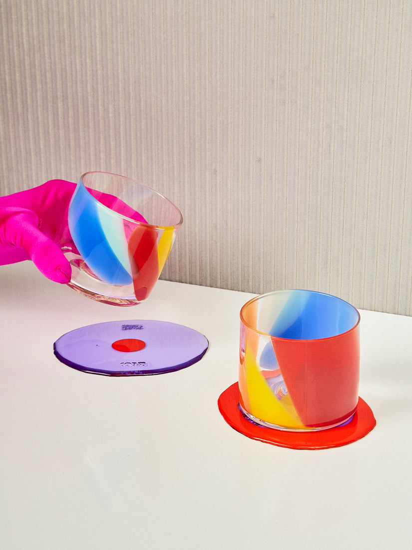 A pair of Rainbow Splash Cups on Table-Mates coasters. One glass is being held up by a gloved hand.