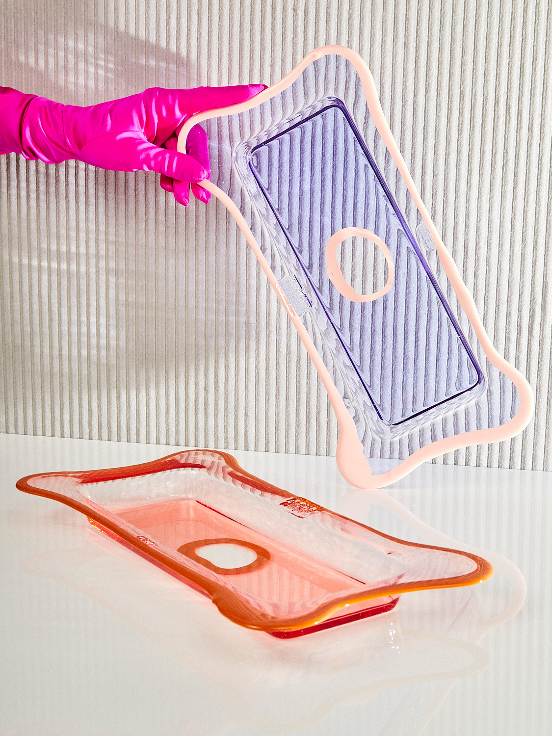 A hand holds up the lavender pink Rectangular Tray above the peach pumpkin tray.