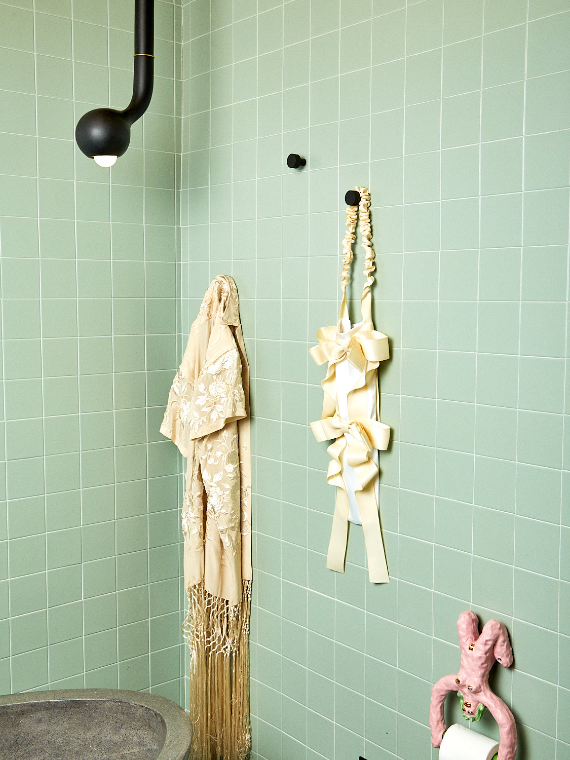 A cream baguette bag hangs in a sage green tiled bathroom.