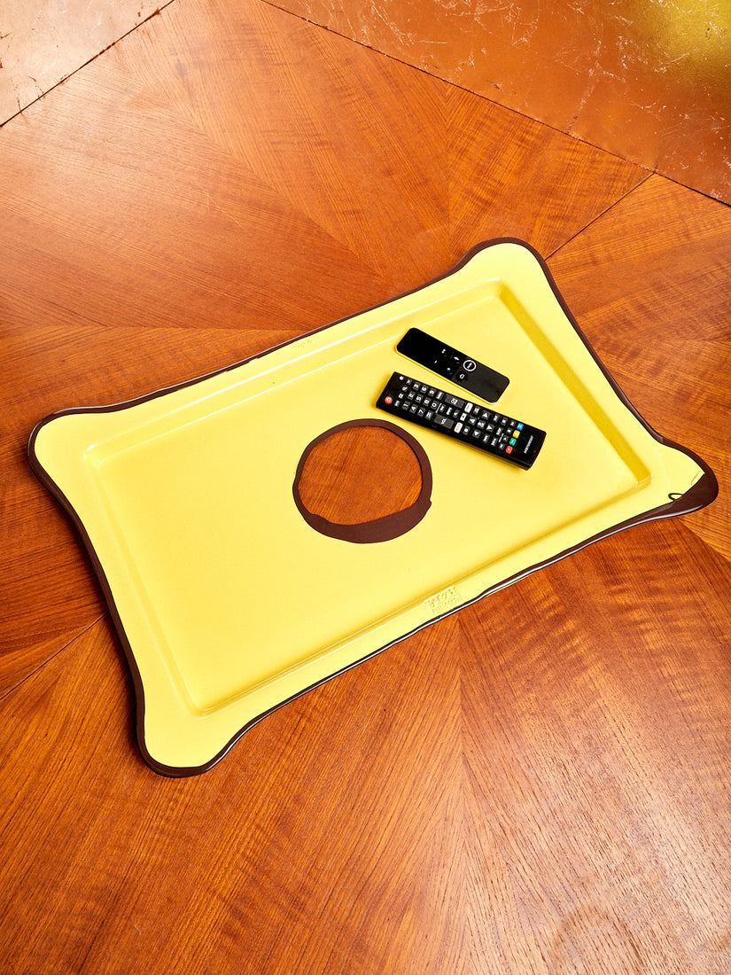 A large rectangular tray in opaque yellow and brwon with two remotes atop.