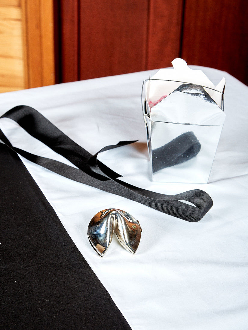 Chrome Fortune Cookie pictured with its silver take out box and black ribbon.