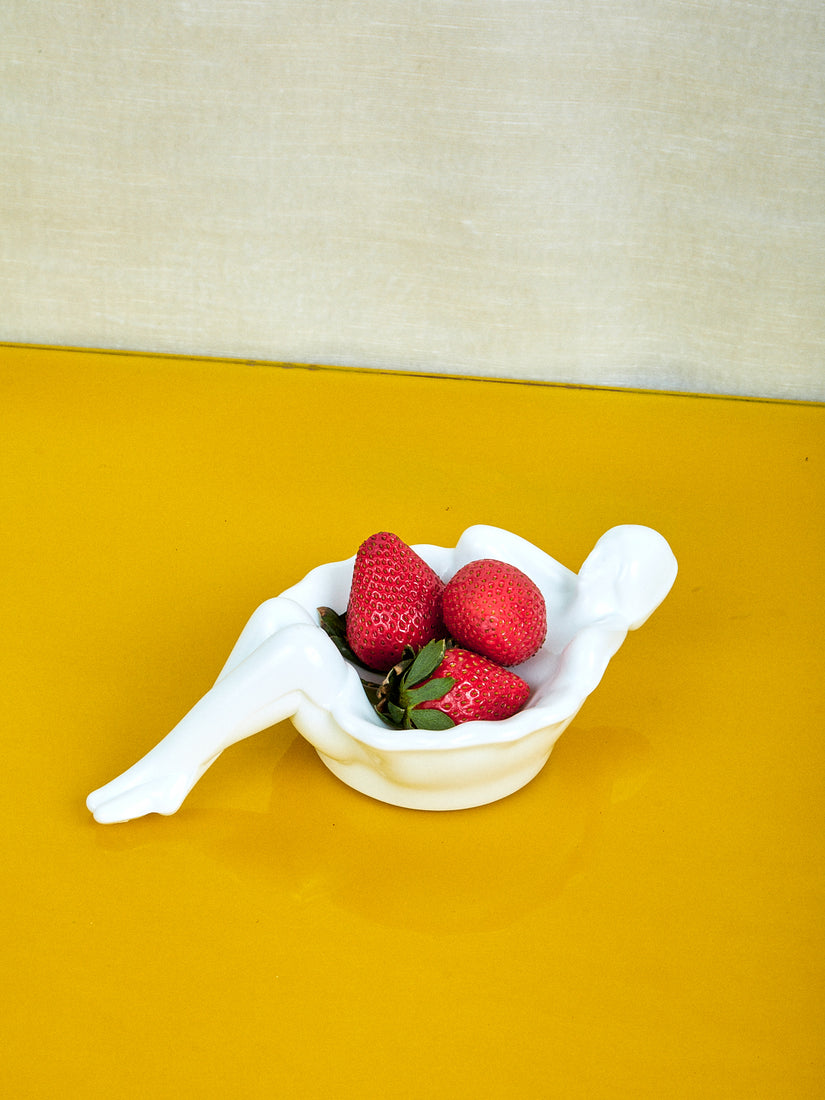 A white bathing lady dish with three strawberries inside.