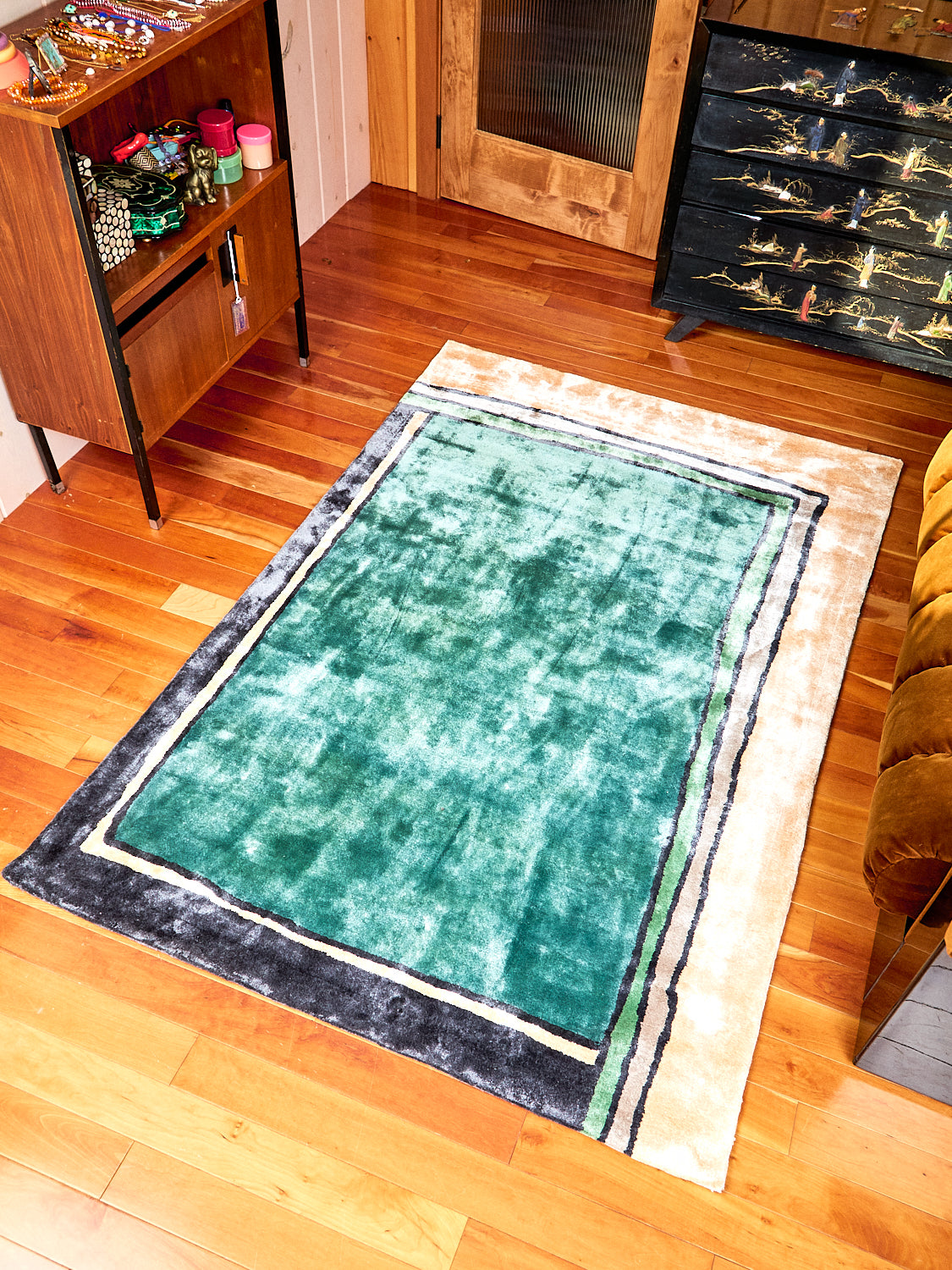 Frames Rug by Cold Picnic displayed on a wooden floor. Rug has colors of teal, black, green and cream. Fabric is a bamboo silk.