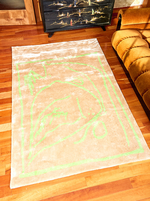 Freya, in Gold Rug by Cold Picnic lays on wooded floor. The Rug is cream with scribbles in lime green all over it. This rug is made of bamboo silk.