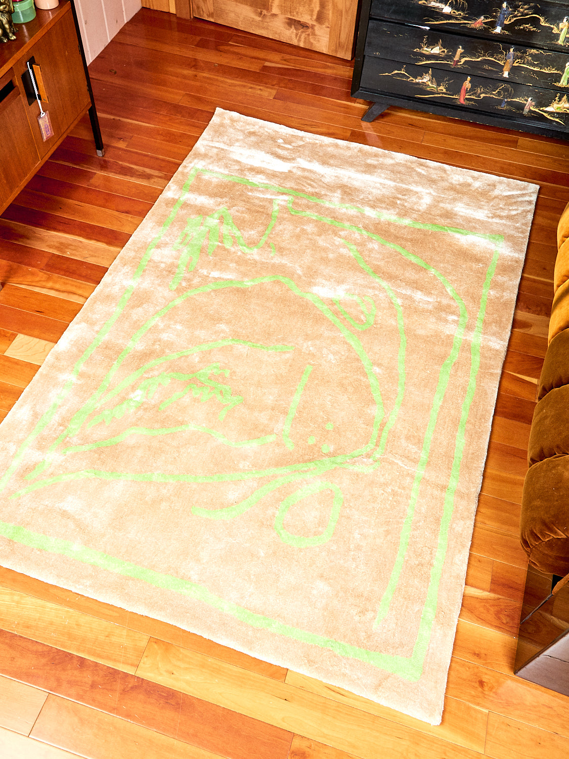 Freya, in Gold Rug by Cold Picnic lays on wooded floor. The Rug is cream with scribbles in lime green all over it. This rug is made of bamboo silk.