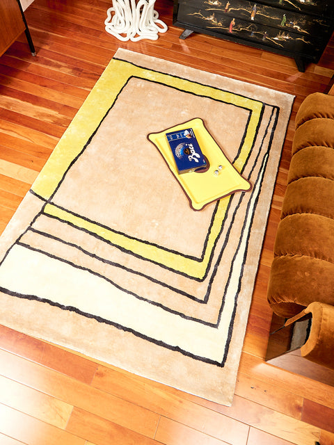 Time Frame Rug by Cold Picnic displayed on a hardwood floor. On the Rug a yellow and brown tray lay. 