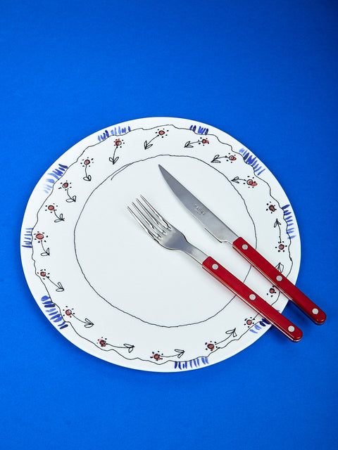 The Marni plate lay on top of a dark blue surface. On the plate a red fork and knife sit.