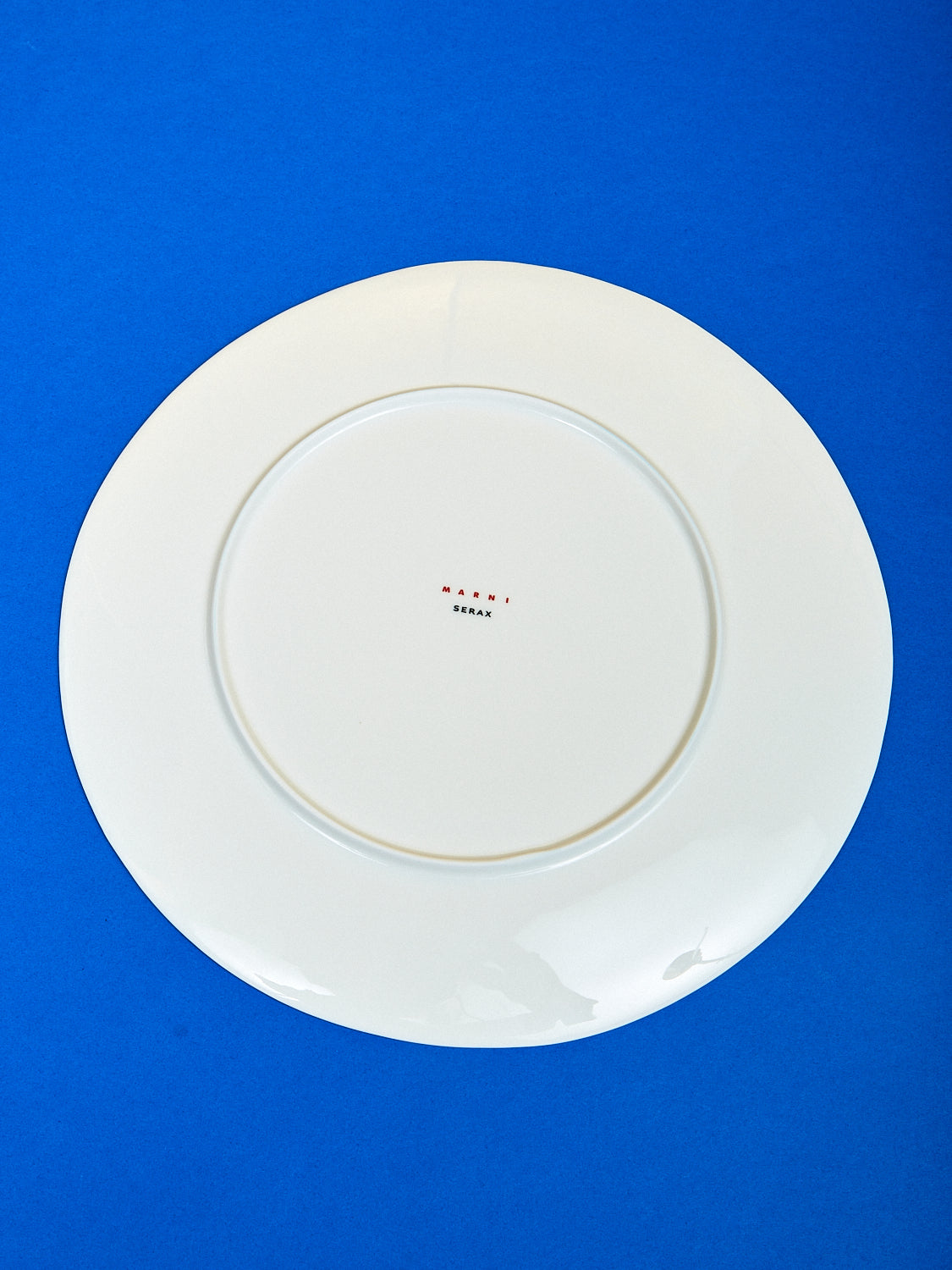 The Marni plate is turned around against the dark blue surface showing the back of the plate.