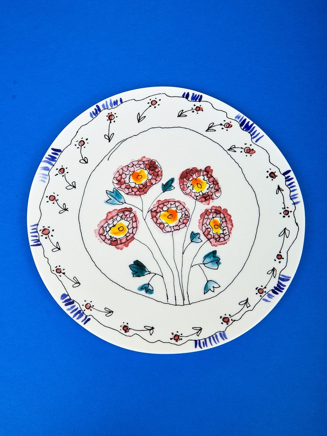 Bird eye view of serving plate by Marni with a dark blue background. On the serving plate there are stencils of flowers and little details all around the edge. 