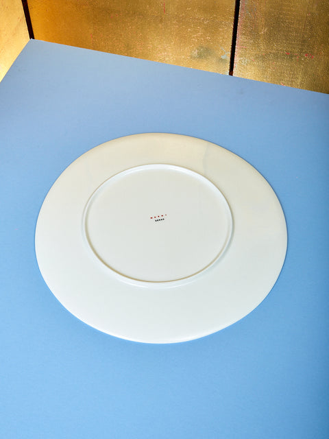 Marni serving plate sits on top of light blue table. The plate is turned around so you can view the details on the back of the plate.