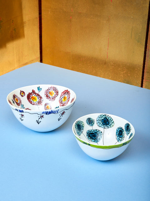 Two bowls lay on top of a blue table. The bowl on the left side is medium and the bowl on the right is small. From the view you can see into the bowl which shows the design and coloring. 