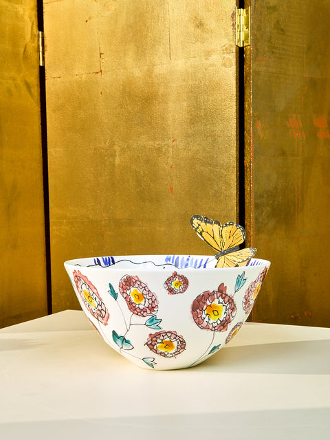 Large Marni bowl sits on top of cream table. On the outside of the bowl there are stencils of flowers with maroon coloring. On the edge of the bowl a fake butterfly sits.