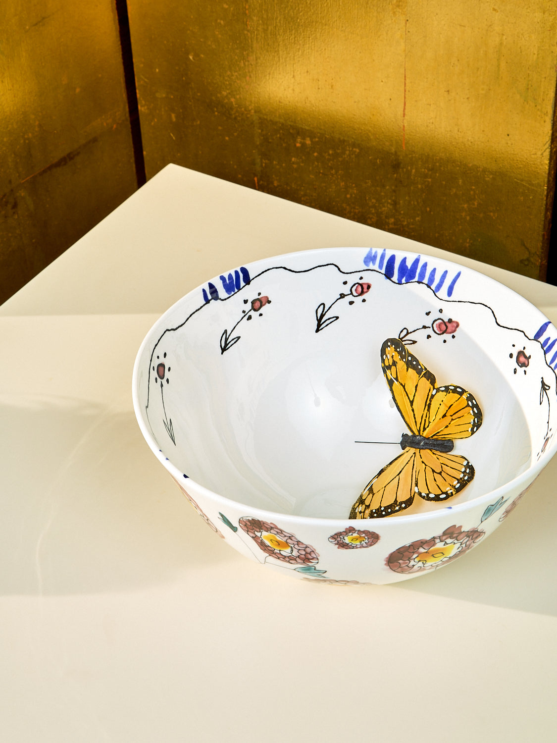 Large serving bowl by Marni sits on top of a cream table. Inside the bowl a fake butterfly is displayed. 