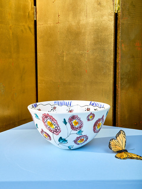 Large serving bowl by Marni sits on a light blue table. Side view showing the stencils of flowers. A fake butterfly sits on the left side of the table.