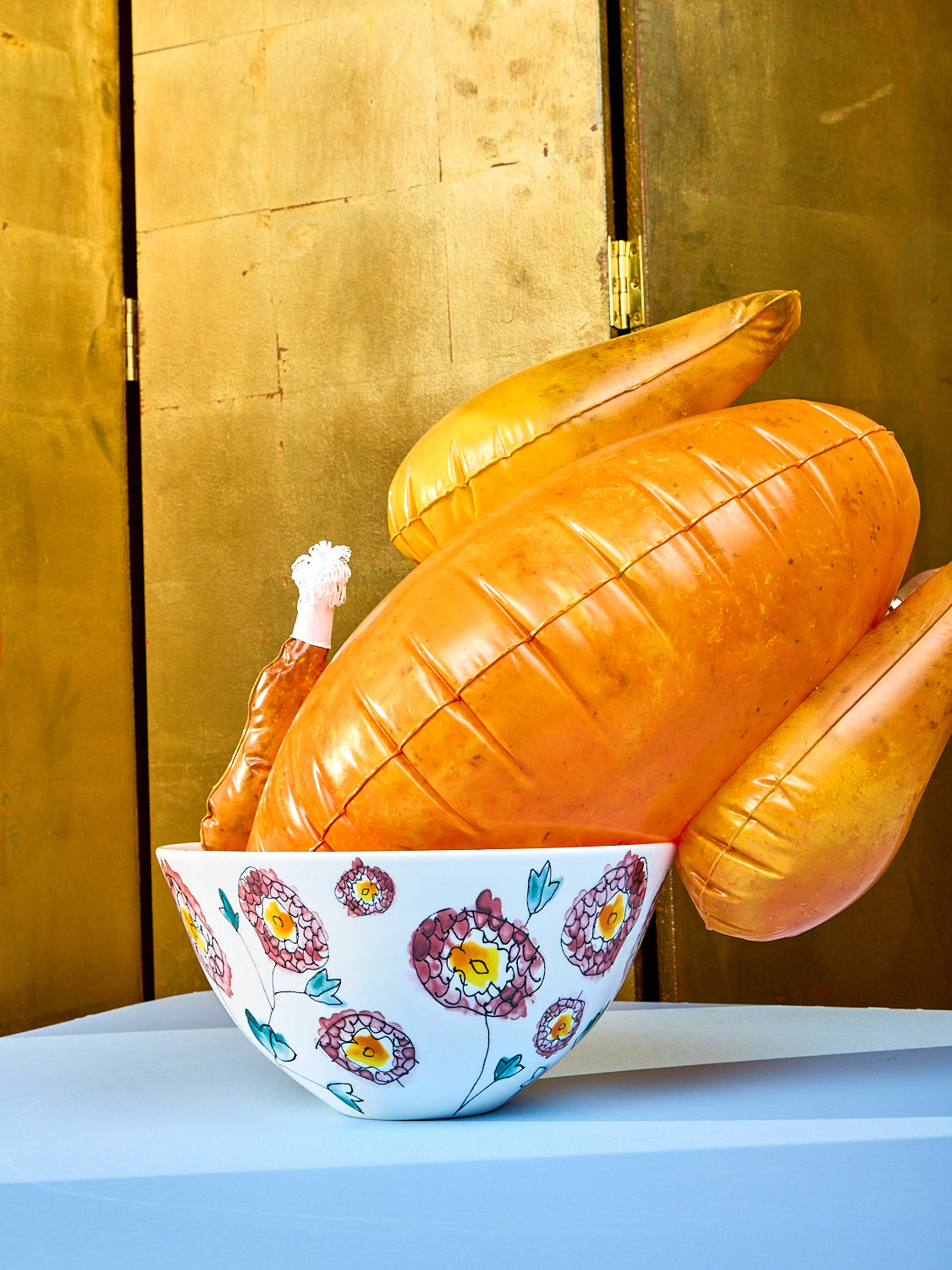 Large serving bowl by Marni sits on a light blue table. Side view showing the stencils of flowers. A fake blown up turkey lays inside the serving bowl. 