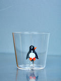 A small cup with a penguin figure made of glass inside sits on a glass table. 