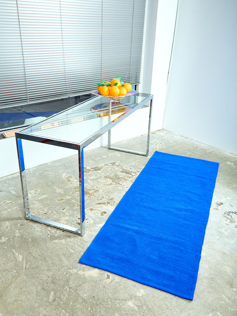 Side angle view looking slightly down at the vintage chrome glass console. On the console, a bowl of Orange Surprise Balls sits on the right side. On top of the cement floor a cobalt blue 2x6 Cotton Runner by Cold Picnic is displayed.