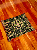 Woven throw pillow in black and green. The pillow sits on a hardwood floor. 