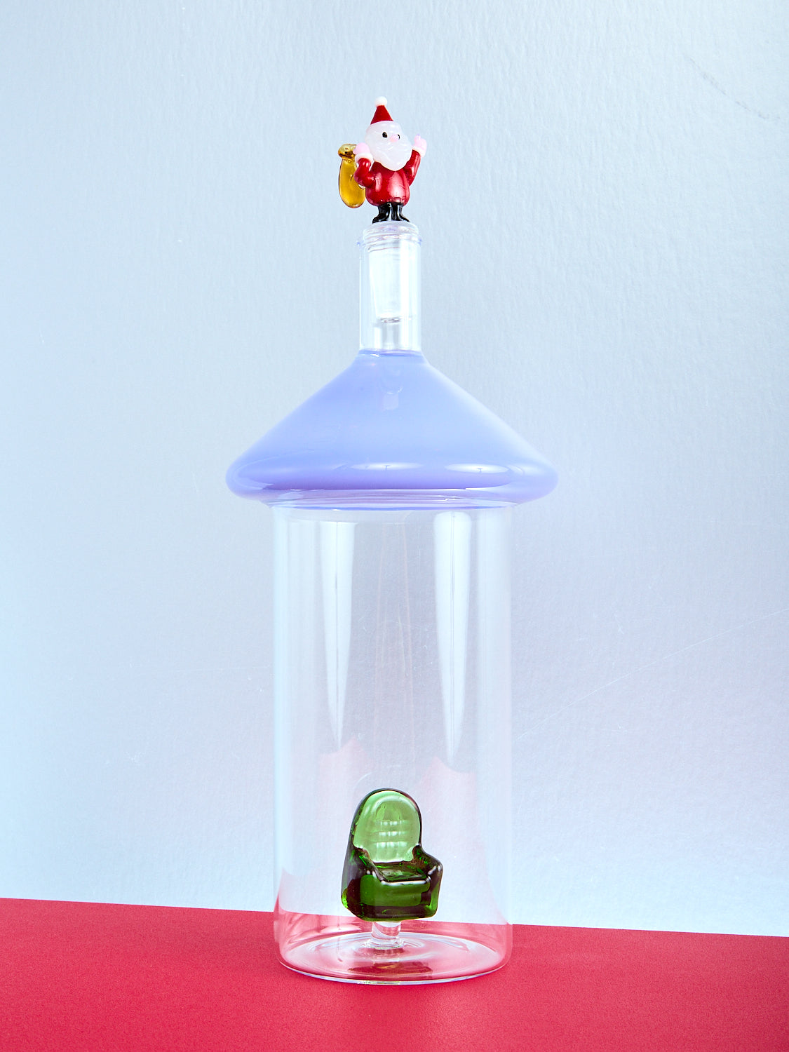 Clear bottle with a blue cap and decorative figure on a red surface with a light blue background
