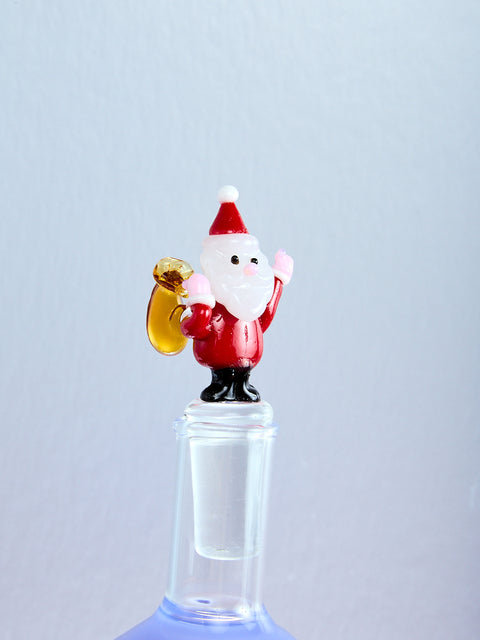 Glass figure of a Santa Claus holding a brown sack on a clear bottle against a light blue background