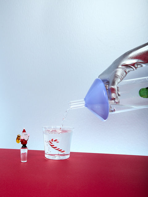 Bottle pouring water into a glass with a small Santa Claus figure on a red surface.
