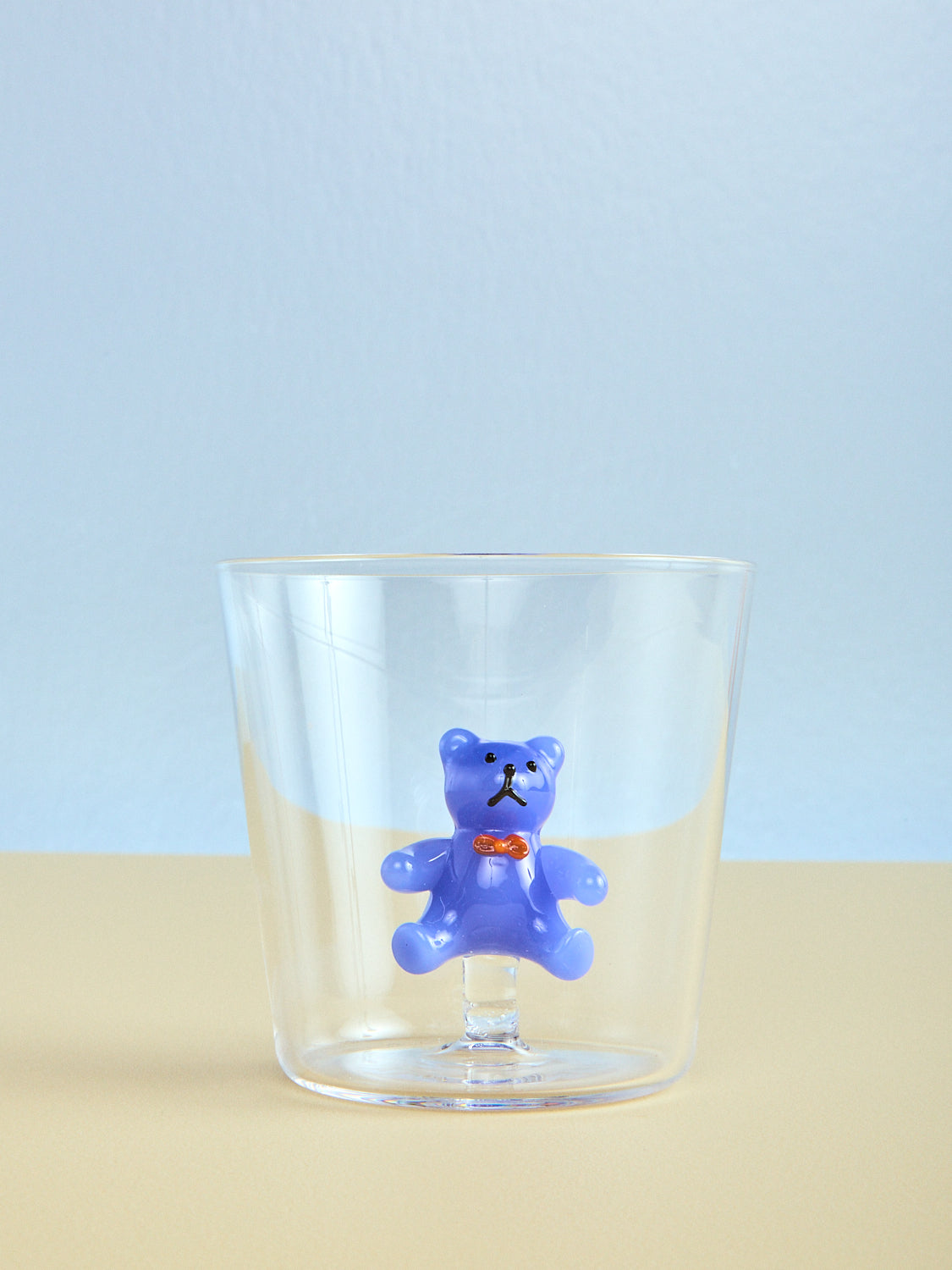 Clear glass with a blue teddy bear figurine on a light blue background