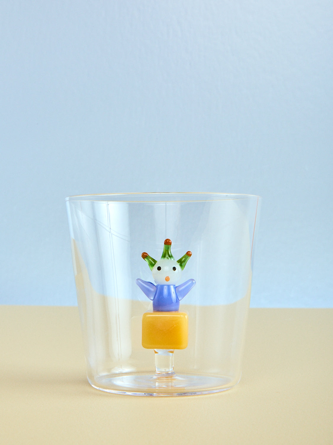 Clear glass with a decorative figure on a beige surface and light blue background