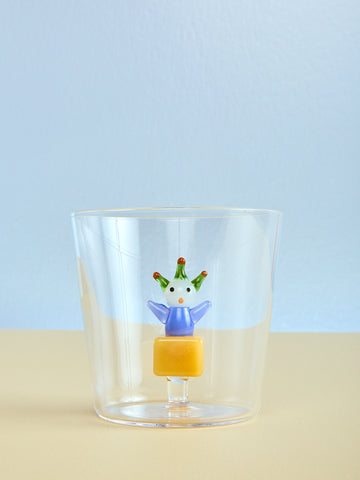 Clear glass with a decorative figure on a beige surface and light blue background