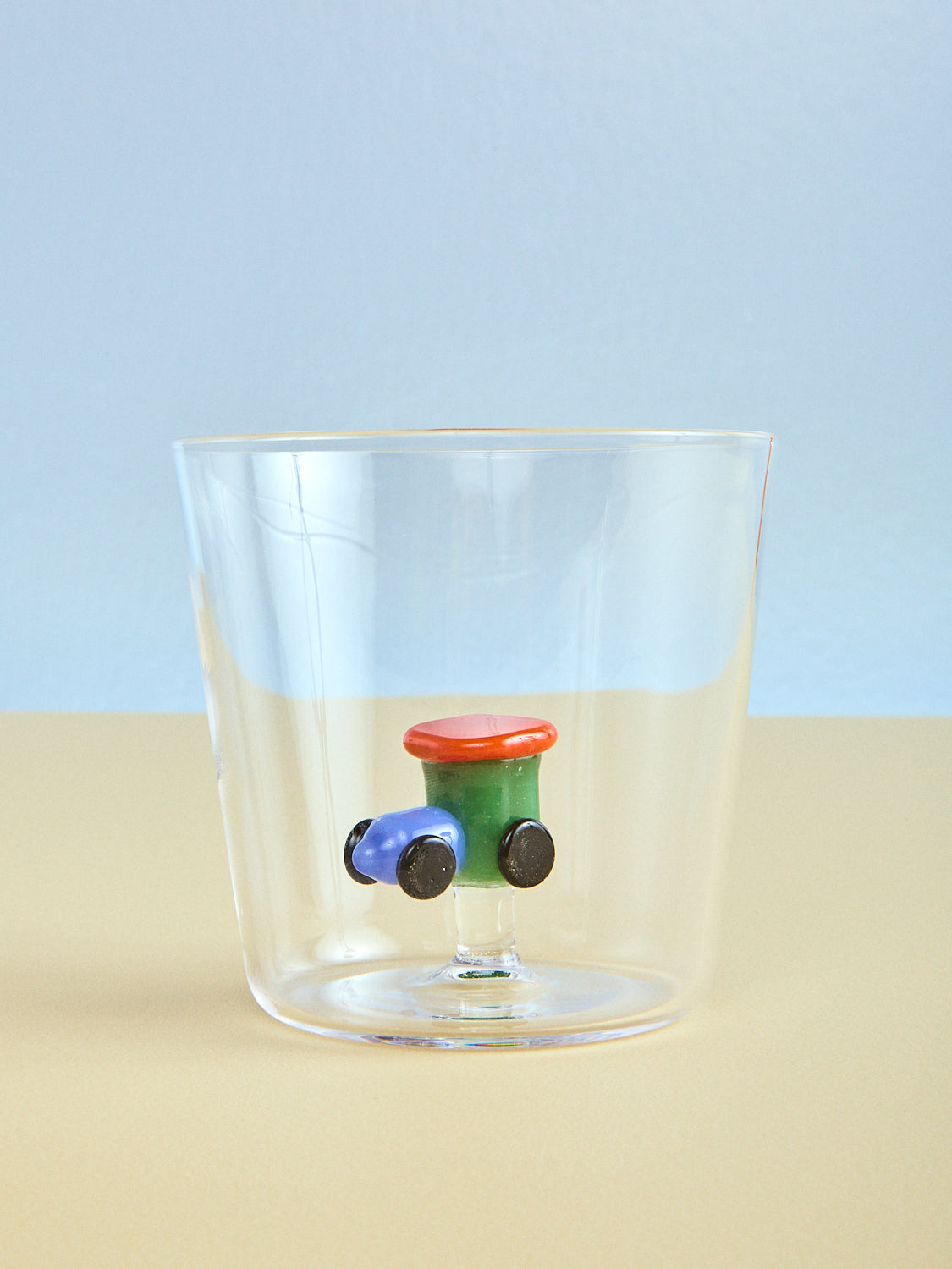 Clear glass with toy train model on a beige surface and light blue background