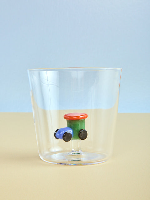 Clear glass with toy train model on a beige surface and light blue background